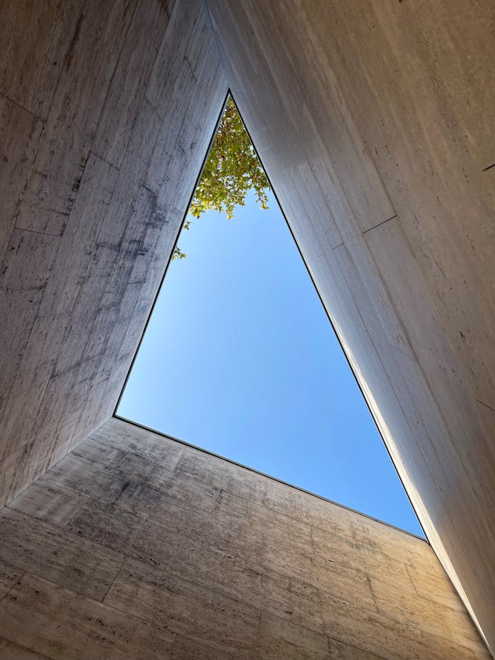 A view of the sky through a triangle opening in minimalist concrete architecture with a hint of greenery.